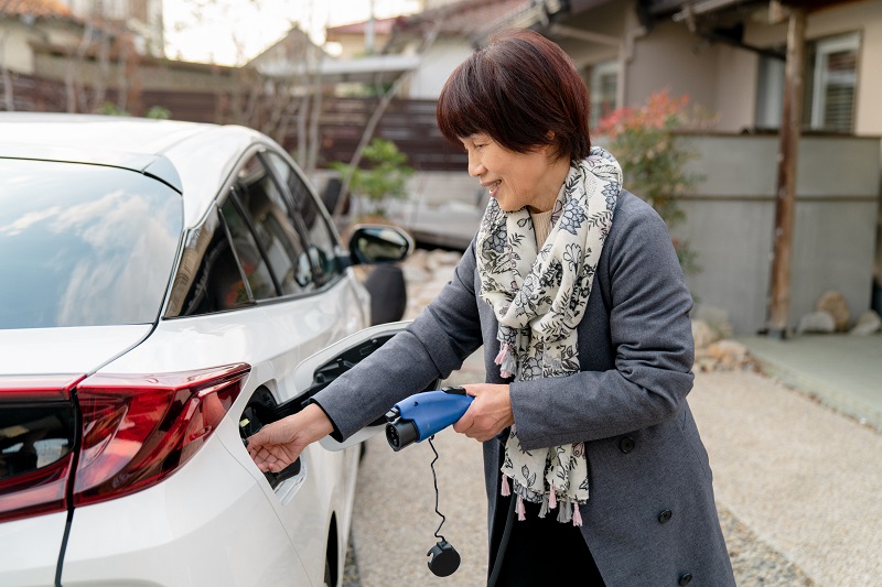 Senior woman charging her electric car at home. Okayama, Japan. 2021